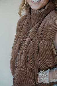 detail view of model wearing the seems so simple puffer vest in the color cocoa. model has the vest paired with the here to stay top in the color cream and the charleston denim.