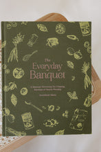 Load image into Gallery viewer, cover photo of &quot;the everyday banquet: a seasonal devotional for creating rhythms of family worship&quot; by SarahRuth Owens. book is shown sitting on a rattan bench.