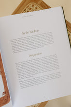 Load image into Gallery viewer, inside page photo of &quot;the everyday banquet: a seasonal devotional for creating rhythms of family worship&quot; by SarahRuth Owens. book is shown sitting on a rattan bench.
