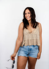 Load image into Gallery viewer, model wearing the moving on top in the color taupe paired with light denim shorts; model is holding a pair of sunglasses in one hand